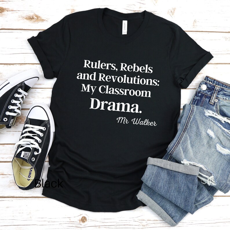 Peut inclure: T-shirt noir avec du texte blanc qui dit "Rulers, Rebels and Revolutions: My Classroom Drama. Mr. Walker"