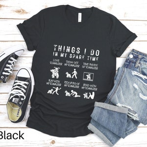 May include: Black t-shirt with a white graphic that says "Things I do in my spare time" and lists activities related to owning a schnauzer. The graphic includes illustrations of a schnauzer.