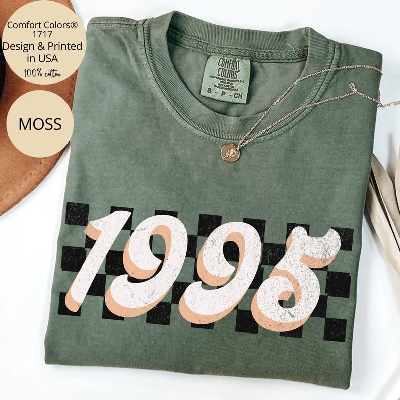 May include: A green t-shirt with a black and white checkered pattern and the year 1995 printed in a retro style font. The shirt is made of 100% cotton and is designed and printed in the USA.