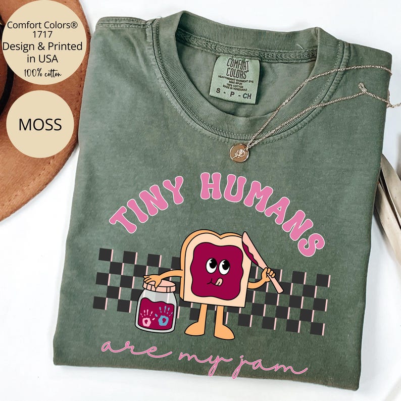 Pu&ograve; includere: T-shirt Comfort Colors verde muschio con la scritta "TINY HUMANS are my jam" in rosa. La grafica presenta un toast a cartoni animati con marmellata, un coltello e un barattolo di marmellata. La maglietta &egrave; 100% cotone.