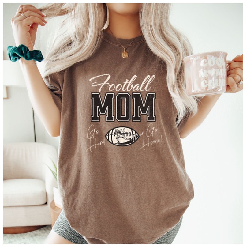 May include: A brown t-shirt with the text "Football MOM" in black letters. The shirt also features a football graphic with the text "Go Hard or Go Home!" in a cursive font.