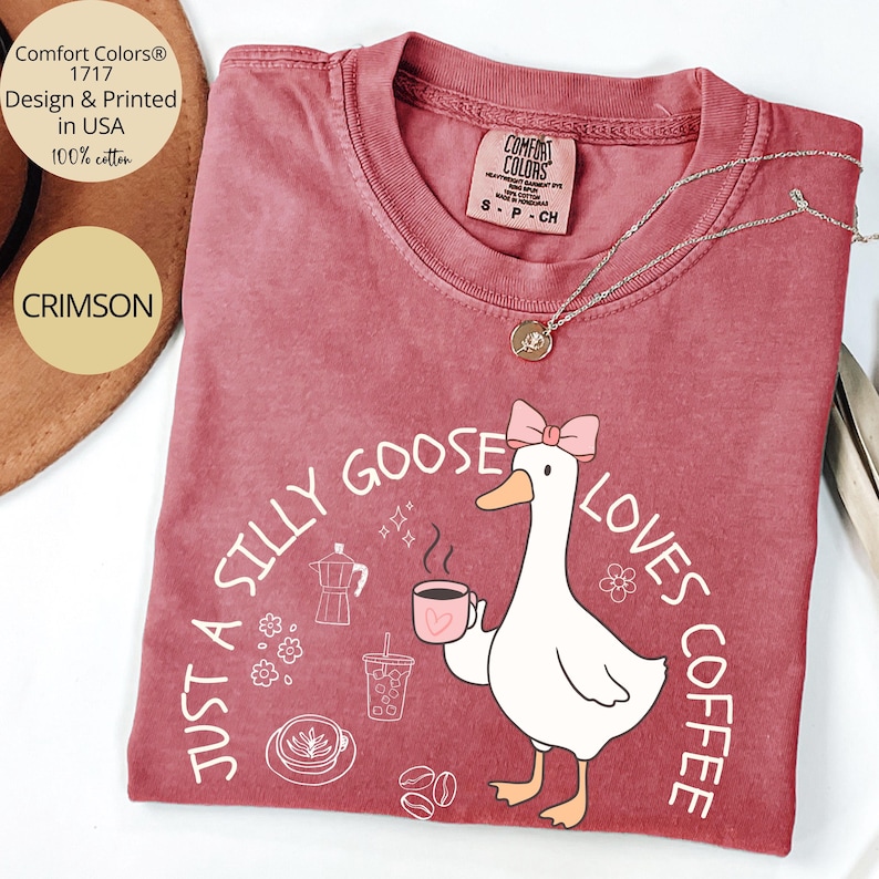 Puede incluir: Camiseta Comfort Colors carmes&iacute; con un gr&aacute;fico de un ganso sosteniendo una taza de caf&eacute;, el texto dice "Just a Silly Goose Loves Coffee". La camiseta es 100% algod&oacute;n y est&aacute; dise&ntilde;ada e impresa en EE. UU.