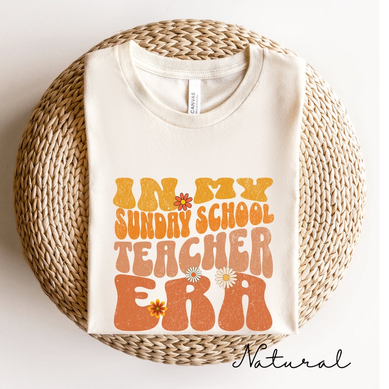 May include: A beige t-shirt with the text "In My Sunday School Teacher Era" in a retro font with orange and yellow colors and floral accents. The text is slightly distressed.