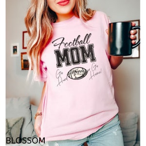 May include: Pink t-shirt with the text "Football Mom" in black with a football graphic and the text "Go Hard or Go Home!" in black cursive.