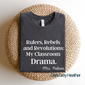 Peut inclure: T-shirt en heather gris fonc&eacute; avec du texte blanc qui dit "Rulers, Rebels and Revolutions: My Classroom Drama. Mrs. Palmer".
