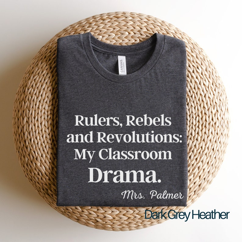 Peut inclure: T-shirt en heather gris fonc&eacute; avec du texte blanc qui dit "Rulers, Rebels and Revolutions: My Classroom Drama. Mrs. Palmer".