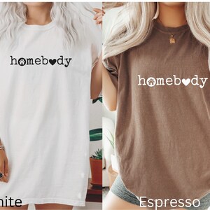 Pode incluir: Duas camisetas oversized com o texto "homebody" e um gr&aacute;fico de uma casa e um cora&ccedil;&atilde;o. A camiseta &agrave; esquerda &eacute; branca e a camiseta &agrave; direita &eacute; expresso.