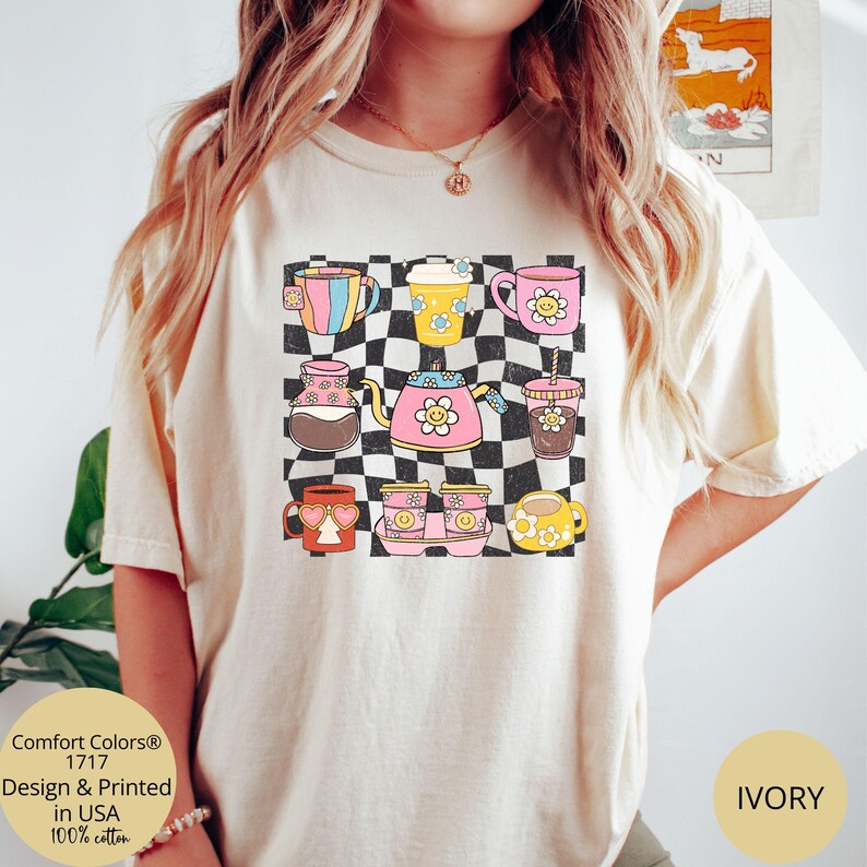 May include: A white t-shirt featuring a graphic of colourful mugs and teapots on a chequered background. The text "Comfort Colors&reg; 1717" is printed in the bottom left corner of the shirt. The text "IVORY" is printed in the bottom right corner of the shirt.