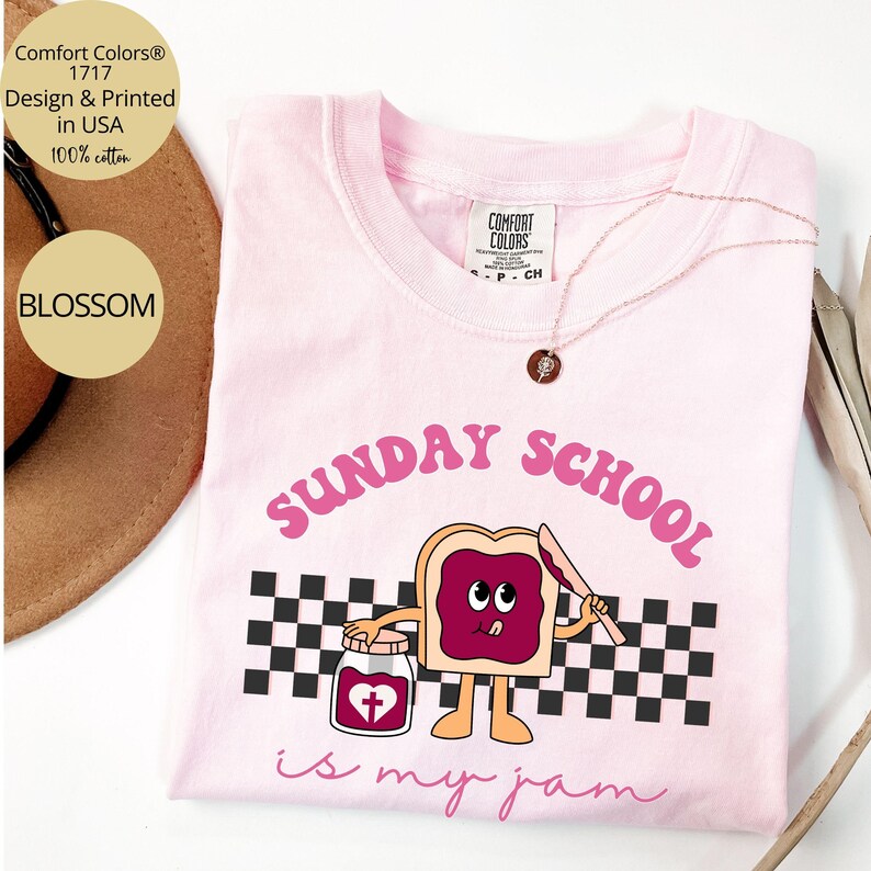 May include: Pink t-shirt with a graphic of a slice of bread with jelly and a cross on a jar. The text "SUNDAY SCHOOL is my jam" is printed on the shirt.