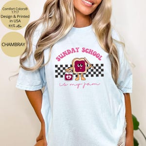 May include: A light blue t-shirt with a graphic of a slice of bread with a knife and a jar of jam. The text "SUNDAY SCHOOL is my jam" is printed on the shirt.