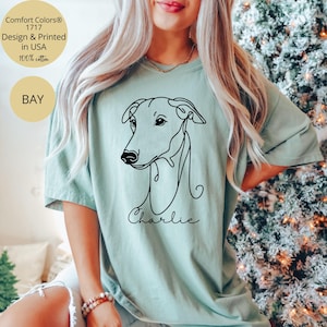 May include: A light green t-shirt featuring a minimalist black line drawing of a dog's head, with the name "Charlie" in script below. The shirt includes text that reads "Comfort Colors 1717 Design & Printed in USA 100% cotton" and the word "BAY".
