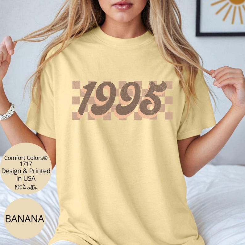 May include: A yellow t-shirt with a brown and peach checkered pattern and the year 1995 in brown text.