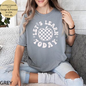 May include: Grey Comfort Colors t-shirt with the text "LET'S LEARN TODAY" in a retro font. The design includes a checkered apple graphic. The shirt is made of 100% cotton.