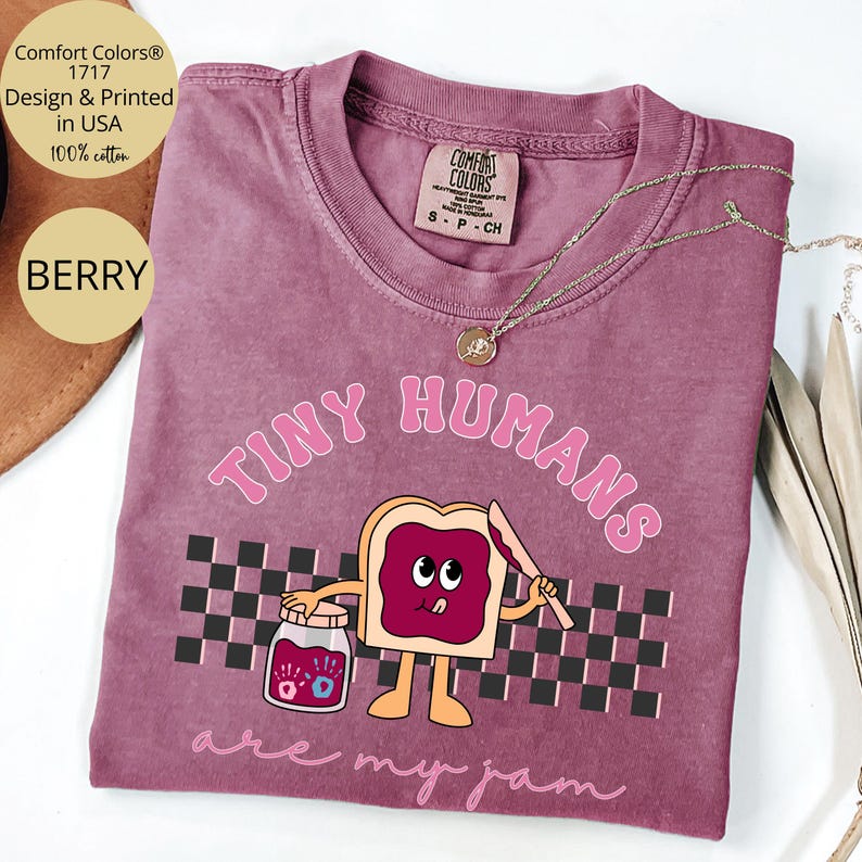 Pu&ograve; includere: T-shirt color bacca con la scritta "TINY HUMANS are my jam" e un'immagine a cartoni animati di una fetta di pane tostato con marmellata. La maglietta presenta anche il logo Comfort Colors ed &egrave; realizzata in 100% cotone.