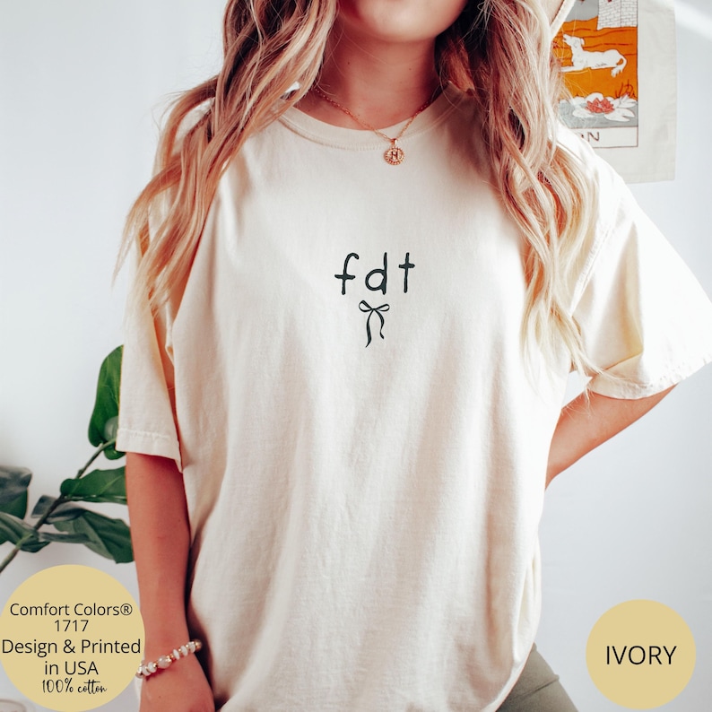 Peut inclure: T-shirt ivoire avec les lettres "fdt" et un motif de n&oelig;ud noir. Le t-shirt est en 100% coton et imprim&eacute; aux &Eacute;tats-Unis. Il s'agit d'un mod&egrave;le Comfort Colors 1717.