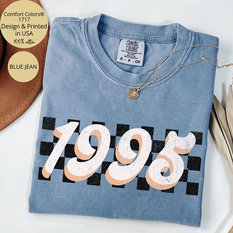 May include: A blue jean t-shirt with a white and peach 1995 graphic on a black and white checkered background. The shirt is made of 100% cotton and is designed and printed in the USA.