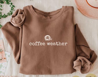 May include: Espresso-colored sweatshirt with the text "coffee weather" and a coffee cup graphic. The sweatshirt is made of 100% cotton and is a light sweatshirt. The image also includes the words "Softness & warmth ALL season".