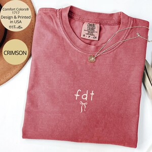 Peut inclure: T-shirt Comfort Colors couleur cramoisi avec l'inscription "fdt" et un n&oelig;ud brod&eacute;. Un collier en argent avec un pendentif est pos&eacute; sur le t-shirt. Il est indiqu&eacute; 100% coton et con&ccedil;u et imprim&eacute; aux &Eacute;tats-Unis.