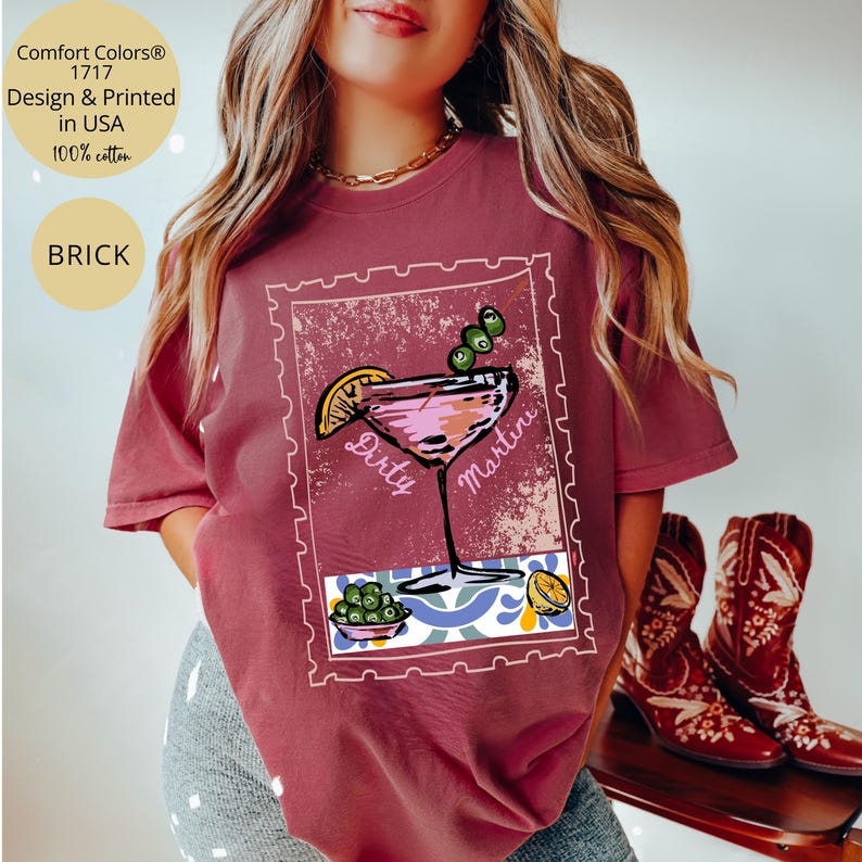 K&ouml;nnte beinhalten: Ziegelrotes T-Shirt mit einer Grafik eines Dirty Martini-Cocktails in einem Briefmarkenrahmen. Das Design umfasst einen rosa Cocktail, Oliven und eine Zitronenscheibe. Das Shirt tr&auml;gt auch den Text "Comfort Colors 1717 Design & Printed in USA 100% cotton".