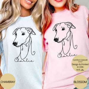 May include: Light blue and pink t-shirts featuring a black line drawing of a dog's head with the name "Charlie" below. The shirts have the text "Comfort Colors 1717 Design & Printed in USA 100% cotton" on them. The shirt colors are "Chambray" and "Blossom".