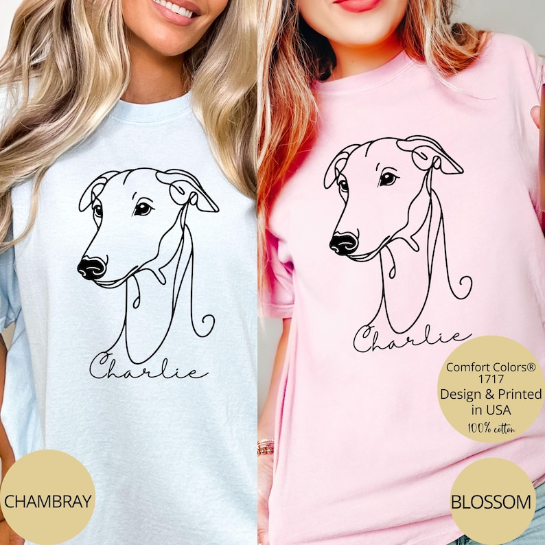 May include: Light blue and pink t-shirts featuring a black line drawing of a dog's head with the name "Charlie" below. The shirts have the text "Comfort Colors 1717 Design & Printed in USA 100% cotton" on them. The shirt colors are "Chambray" and "Blossom".
