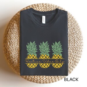 May include: Black t-shirt featuring a design of three yellow pineapples with green tops and the text "Positive Vibes Only" in a brown rectangle.