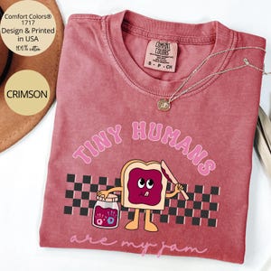Pu&ograve; includere: T-shirt Comfort Colors color cremisi con la scritta "TINY HUMANS are my jam" e un'immagine a cartoni animati di pane tostato con marmellata. La maglietta &egrave; 100% cotone e progettata e stampata negli Stati Uniti.