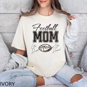 May include: A cream colored t-shirt with the text "Football Mom" in black with a football graphic and the text "Go Hard or Go Home!" in black.