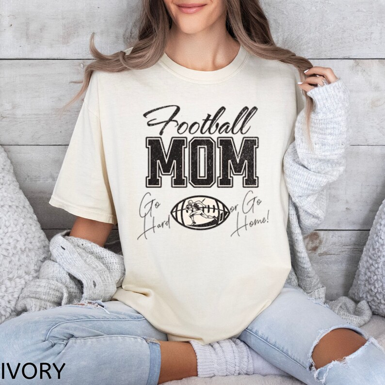 May include: A cream colored t-shirt with the text "Football Mom" in black with a football graphic and the text "Go Hard or Go Home!" in black.