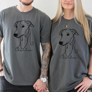 May include: Two charcoal gray t-shirts featuring a minimalist line drawing of a dog's head. Below the drawing, the name "Charlie" is written in cursive. The shirts are a matching set, perfect for dog lovers.