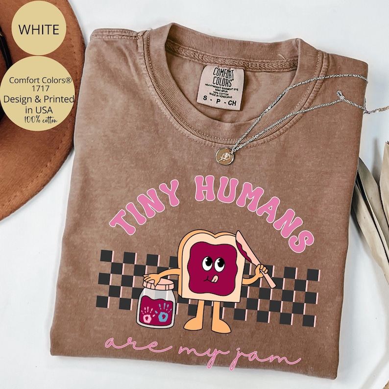 Pu&ograve; includere: T-shirt Comfort Colors marrone con la scritta rosa "TINY HUMANS are my jam". La grafica presenta un toast dei cartoni animati con marmellata e un barattolo di marmellata. La maglietta &egrave; realizzata in 100% cotone.