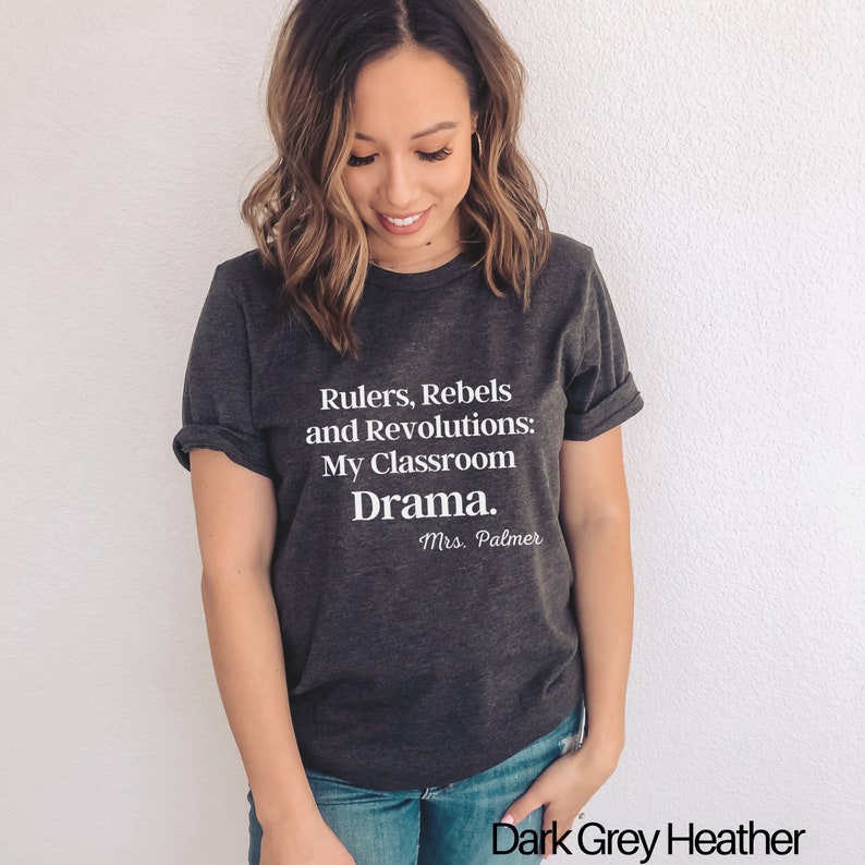 Peut inclure: T-shirt en jersey gris fonc&eacute; avec un texte blanc qui dit "Rulers, Rebels and Revolutions: My Classroom Drama. Mrs. Palmer".