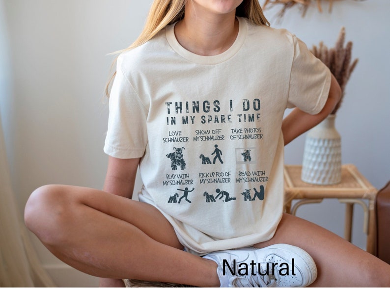 May include: A beige t-shirt with a graphic print that says "Things I do in my spare time" and lists activities related to owning a Schnauzer dog. The text is in a distressed font style.