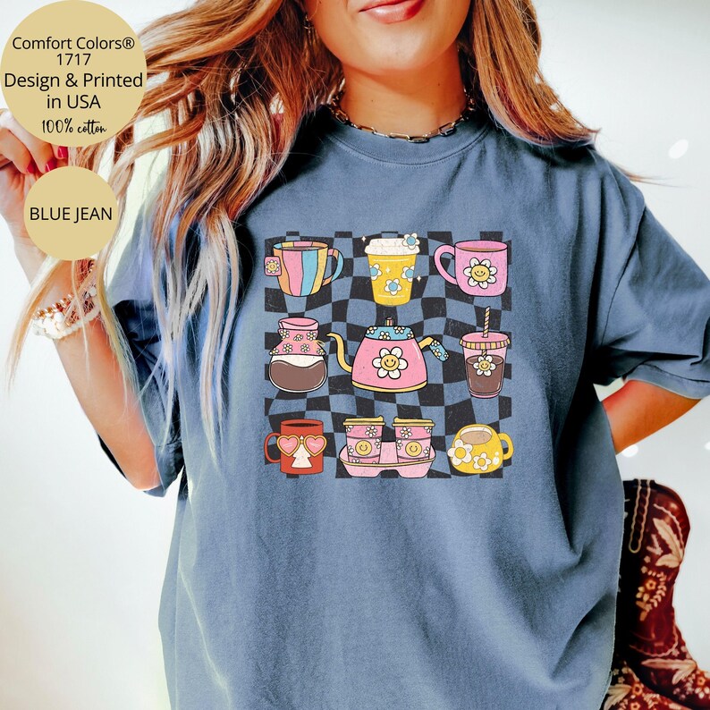 May include: A blue jean t-shirt featuring a graphic of assorted coffee cups and mugs against a checkered backdrop. The text "Comfort Colors&reg; 1717 Design & Printed in USA 100% cotton BLUE JEAN" is printed on the shirt.