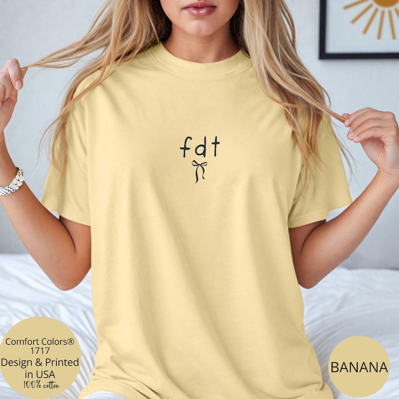 Peut inclure: T-shirt jaune clair avec le texte "fdt" et un motif de n&oelig;ud noir. Fabriqu&eacute; en 100% coton et imprim&eacute; aux &Eacute;tats-Unis. Le t-shirt est un mod&egrave;le Comfort Colors 1717.