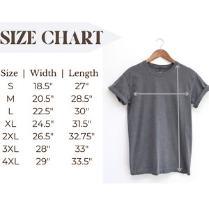 Puede incluir: Una camiseta gris oscuro colgada de una percha de madera. La imagen incluye una tabla de tallas con medidas en pulgadas para el ancho y el largo, que van desde la talla peque&ntilde;a hasta la 4XL. Las medidas tambi&eacute;n se muestran en cm.