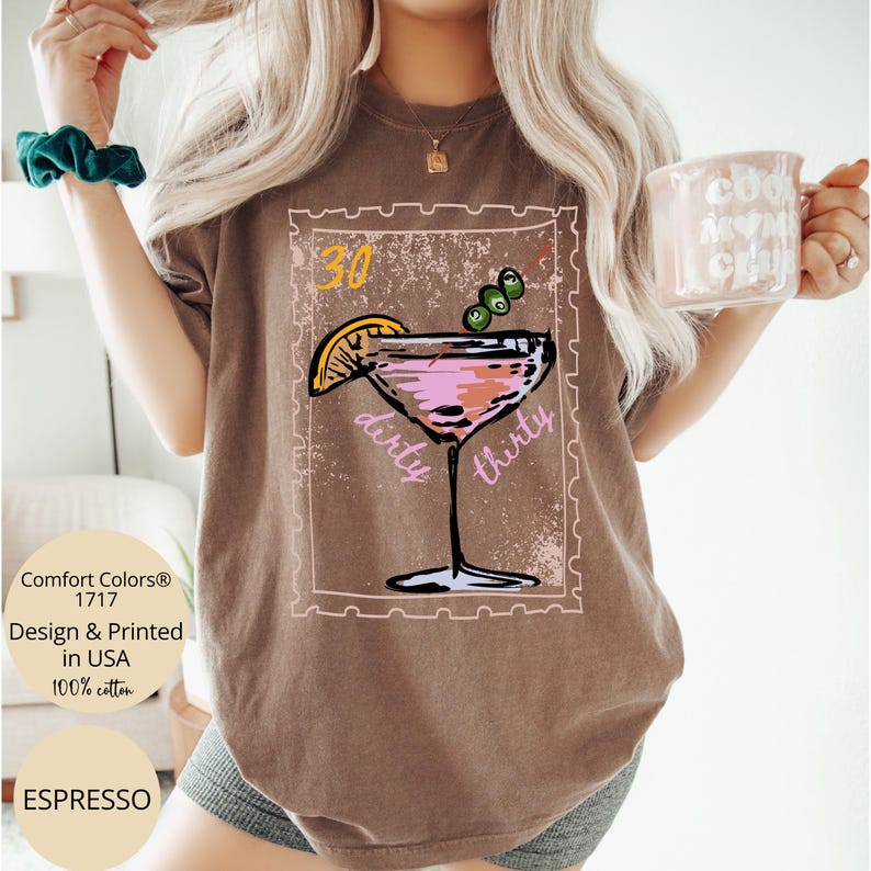 May include: Espresso-colored t-shirt featuring a cocktail design with the words "dirty thirty." The design includes a martini glass with a lemon slice and olives. The shirt also has the text "Comfort Colors 1717 Design & Printed in USA 100% cotton."