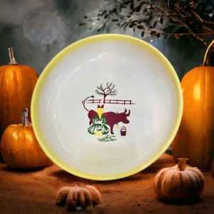 May include: A white ceramic bowl with a yellow rim features a vintage illustration of a girl and a cow in a farm setting. The bowl is surrounded by pumpkins.