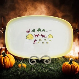 May include: A white oval serving platter with a yellow rim features a hand-painted scene of a farm with two horses, hay bales, trees, and a small red barn. The platter is on a decorative metal stand.