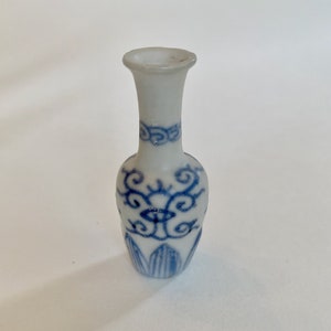 May include: A small white porcelain vase with a blue and white floral design. The vase has a narrow neck and a rounded body.