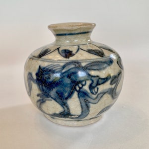 Peut inclure: Un petit vase rond en céramique blanche avec des motifs floraux bleus et blancs. Le vase a un glaçage craquelé et un bord légèrement ébréché.