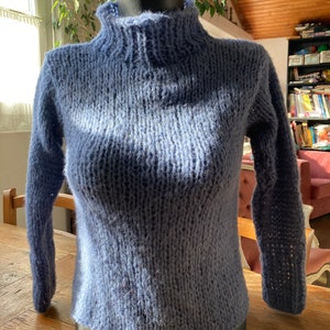 Könnte beinhalten: Ein weicher, blauer Strickpullover mit hohem Kragen und langen Ärmeln.