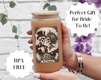 May include: A brown glass candle jar with a wooden lid. The candle has a label with a black and white illustration of two skeletons dressed in wedding attire. The label reads "Till Death".