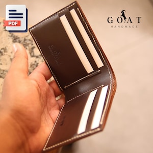 Puede incluir: Cartera de cuero marrón abierta con costuras blancas y múltiples ranuras para tarjetas. La cartera tiene el texto "GOAT HANDMADE" y un logotipo de silueta de cabra. La cartera está abierta, mostrando las ranuras interiores.
