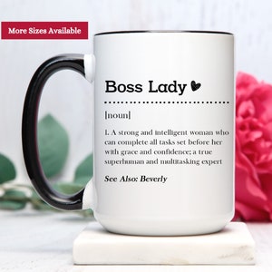 May include: A white ceramic mug with a black handle and rim. The front features black text that reads: Boss Lady [noun] 1. A strong and intelligent woman who can complete all tasks set before her with grace and confidence; a true superhuman and multitasking expert. See Also: Beverly.