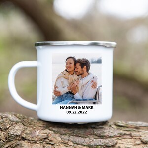 K&ouml;nnte beinhalten: Wei&szlig;e Emailtasse mit einem Foto eines sich umarmenden Paares. Die Tasse hat einen silbernen Rand und den Text "HANNAH & MARK 09.22.2022" unten aufgedruckt.