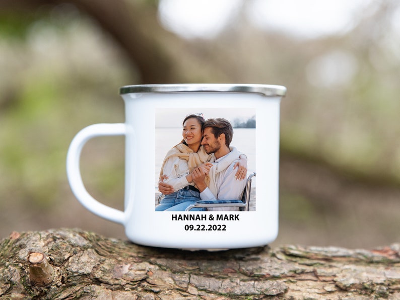 K&ouml;nnte beinhalten: Wei&szlig;e Emailtasse mit einem Foto eines sich umarmenden Paares. Die Tasse hat einen silbernen Rand und den Text "HANNAH & MARK 09.22.2022" unten aufgedruckt.