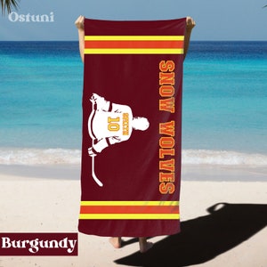 May include: Burgundy beach towel with a hockey player silhouette and the text "SNOW WOLVES" in white. The player is wearing a jersey with the number "10" and the name "SMITH" on the back.