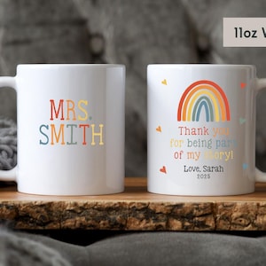 May include: Two white ceramic mugs with rainbow designs. One mug says "MRS. SMITH" in colorful letters. The other mug has a rainbow and the text "Thank you for being part of my story! Love, Sarah 2025".
