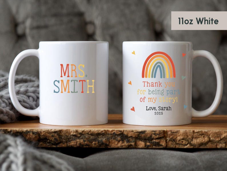 May include: Two white ceramic mugs with rainbow designs. One mug says "MRS. SMITH" in colorful letters. The other mug has a rainbow and the text "Thank you for being part of my story! Love, Sarah 2025".